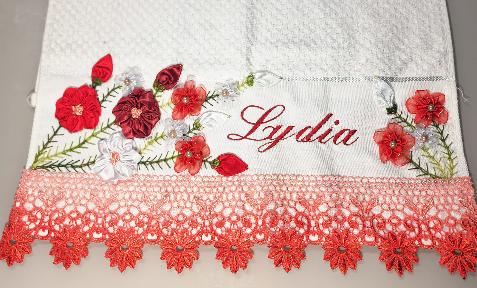 Pano de prato bordado com flores vermelhas e o nome Lydia, com barrado de crochê vermelho