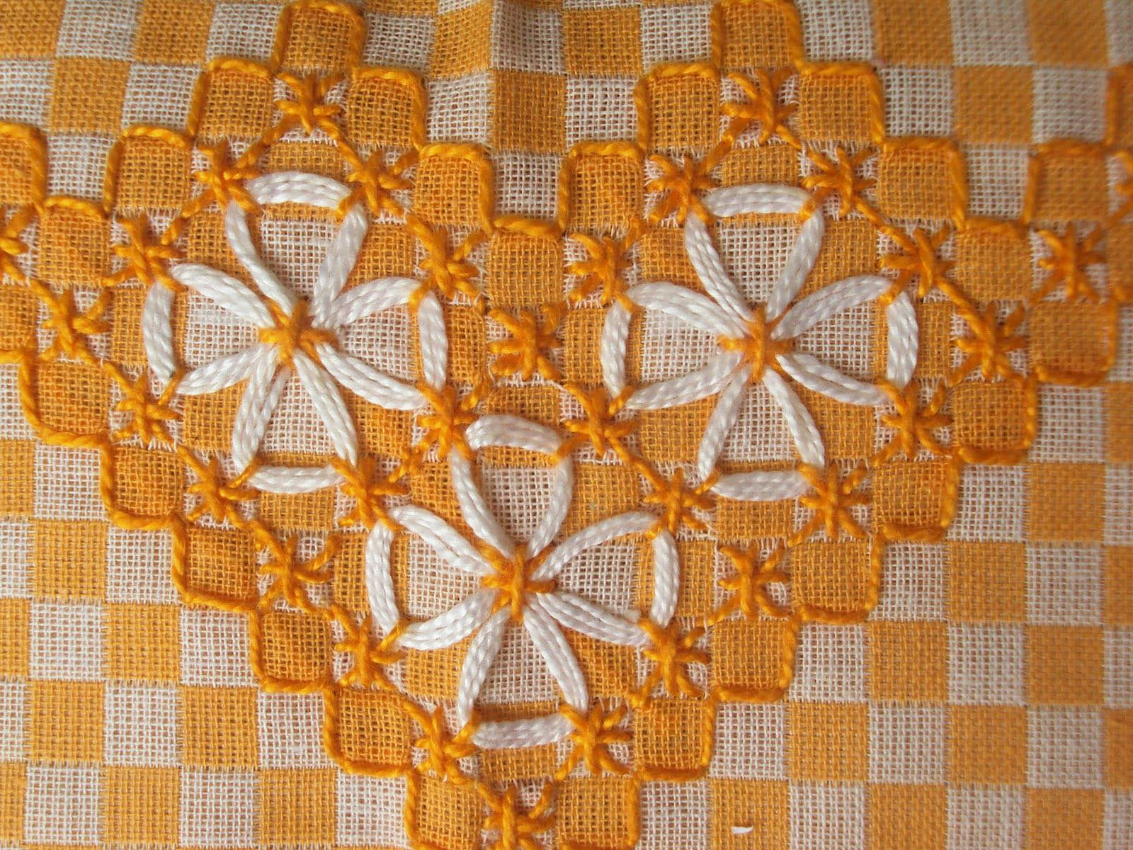 Detalhe de bordado branco em forma de flores sobre tecido xadrez amarelo