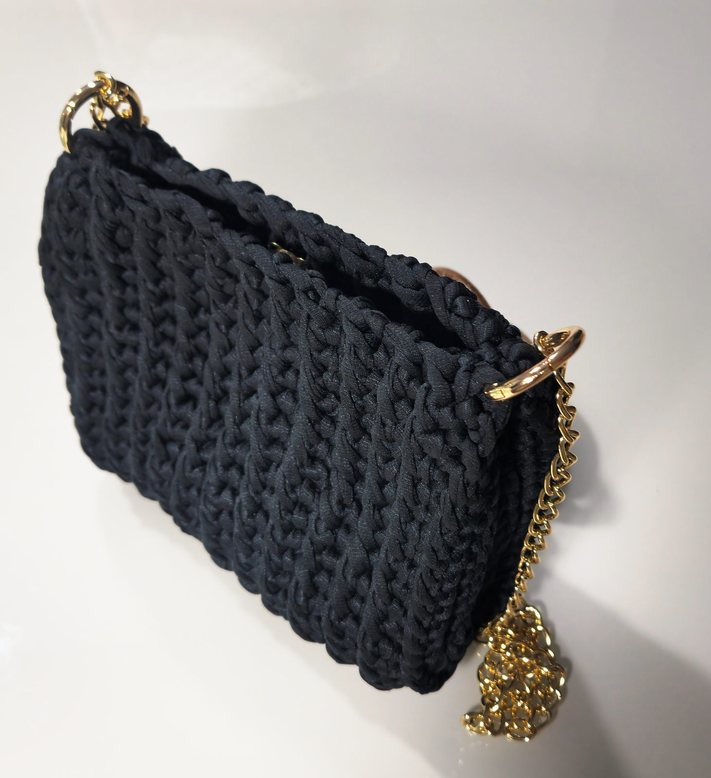 Bolsa preta de crochê com alça de corrente dourada, sobre uma mesa branca