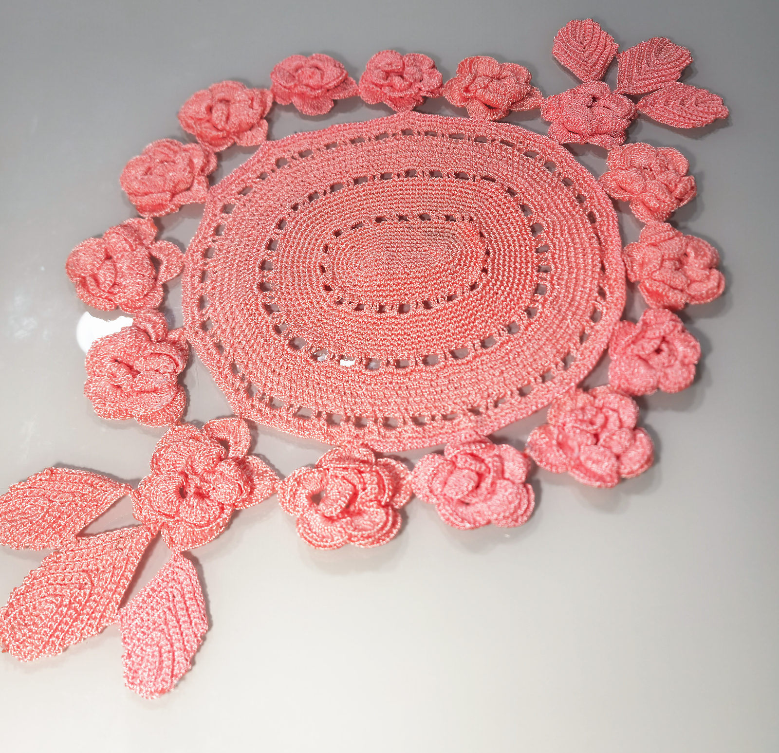 Centro de mesa oval de crochê cor de salmão, rodeado de rosas e folhas também de crochê