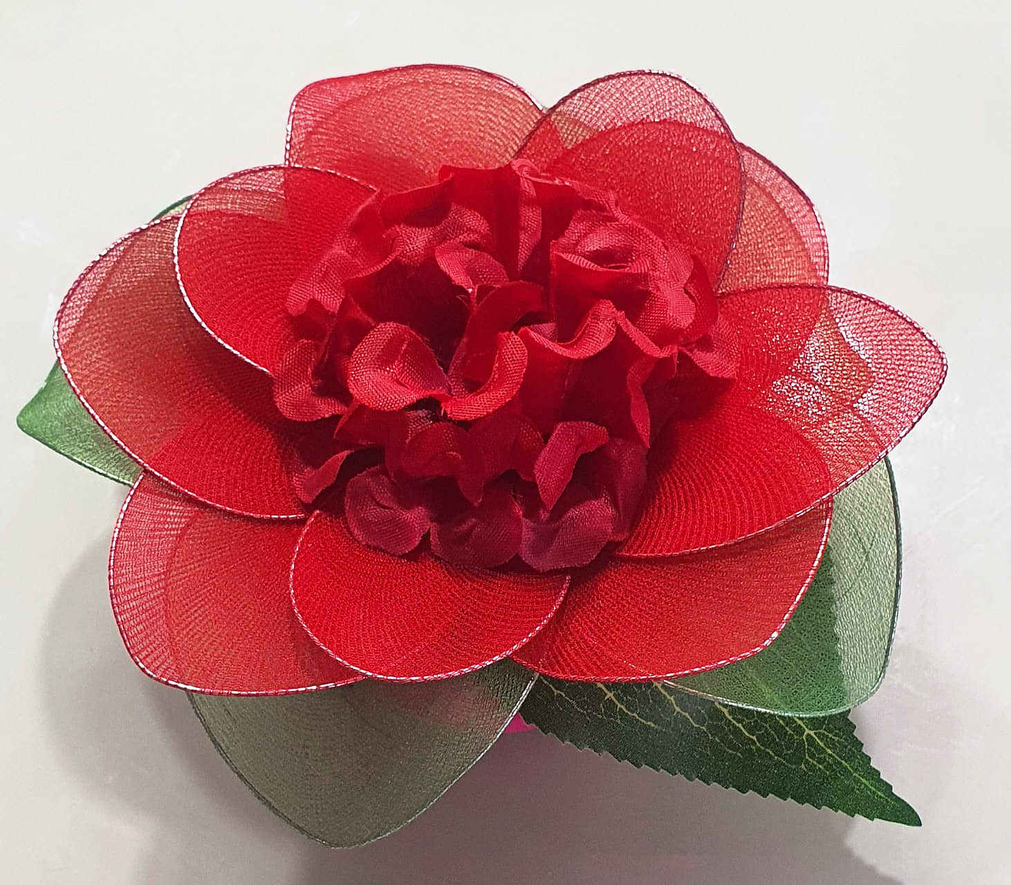 Flor vermelha de meia de seda, com pétalas transparentes, miolo cheio e folhas verdes